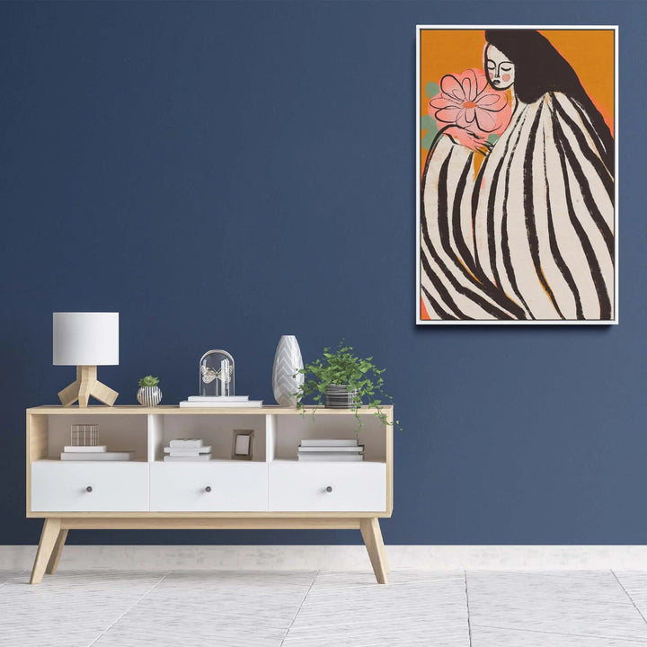 A framed print titled a silent moment by Treechild of a woman in black and white stripes holding a pink flower on orange