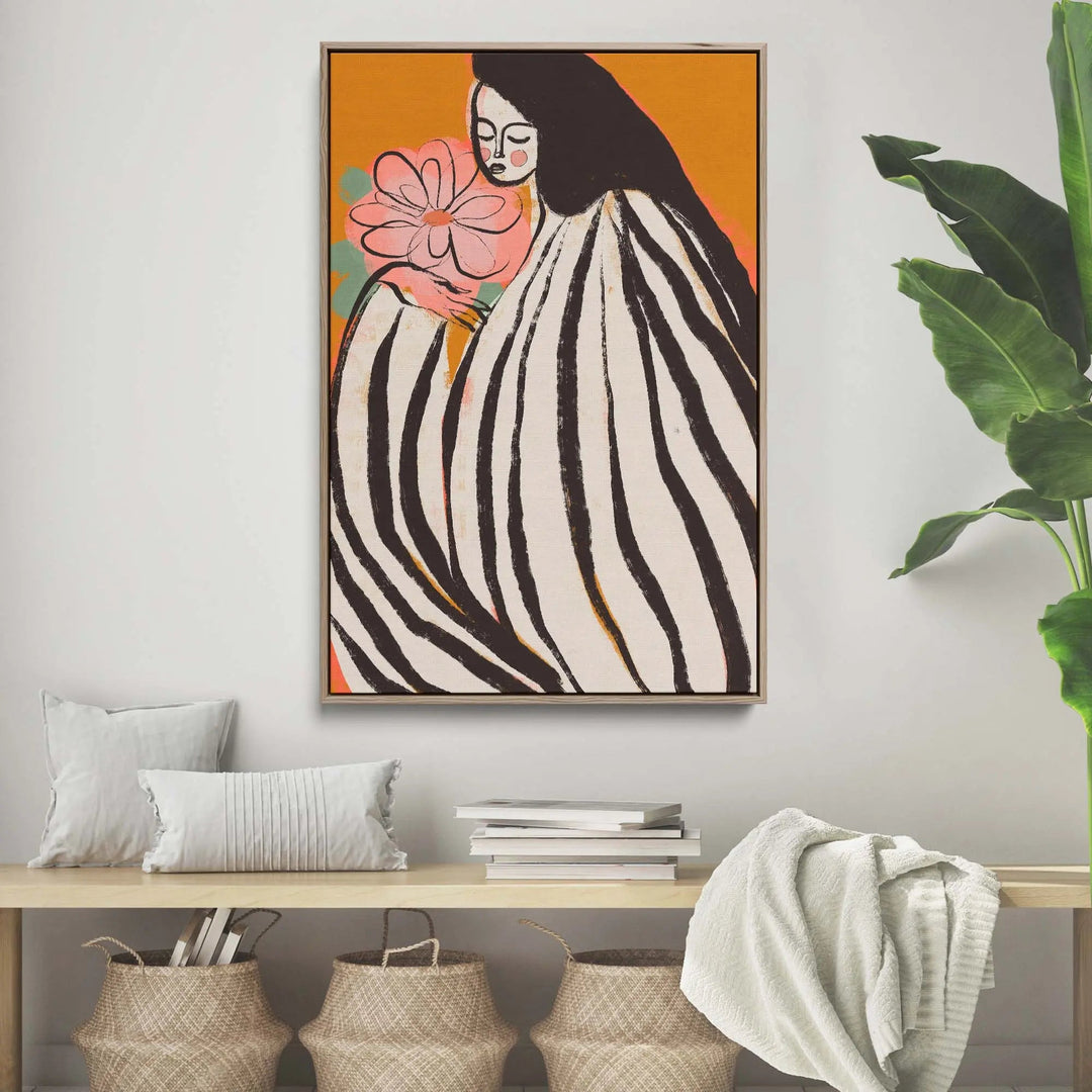 A framed print titled a silent moment by treechild featuring a woman in black and white stripes holding a pink flower on orange background