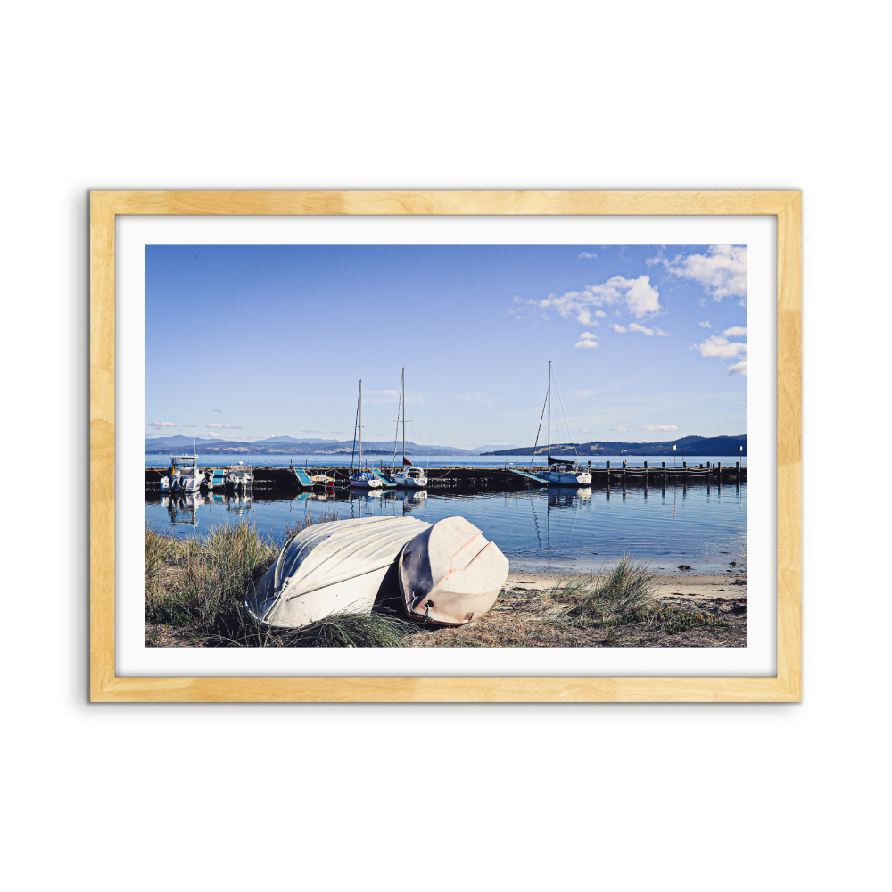 Light wood-framed photographic print of alonnah harbor scene with boats calm water and blue sky by edwina cameron