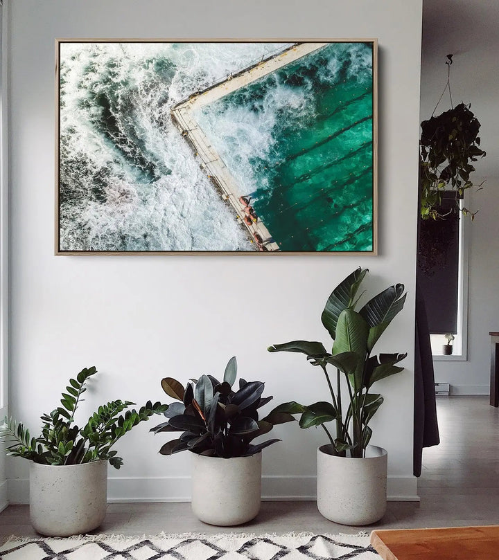 A framed fine art print of a turquoise ocean pool with white waves in a gold-colored frame for ocean swimming decor