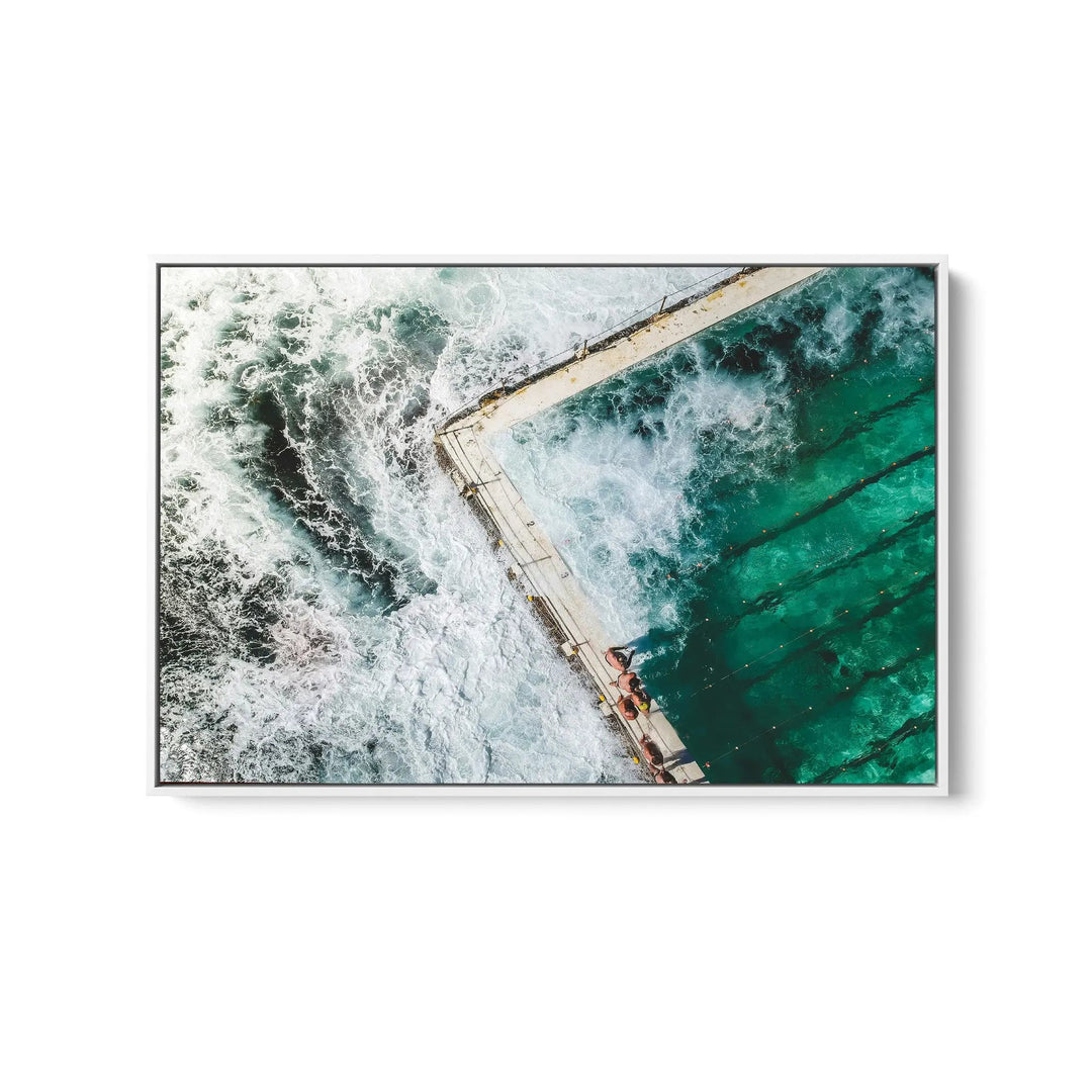 A framed fine art print of a turquoise ocean pool with white waves and two people sitting on a concrete edge