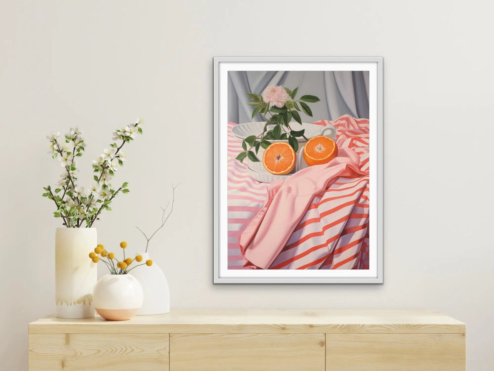 A framed still life painting titled cut orange featuring two orange halves a pink rose and striped pink and white fabric