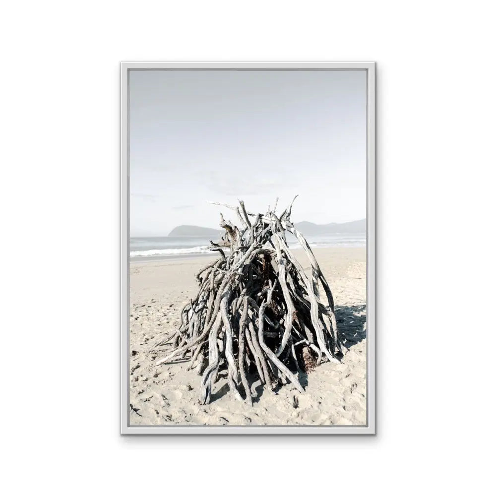 A framed photographic print by Edwina Cameron of bleached driftwood tangled on a sandy beach in soft natural tones