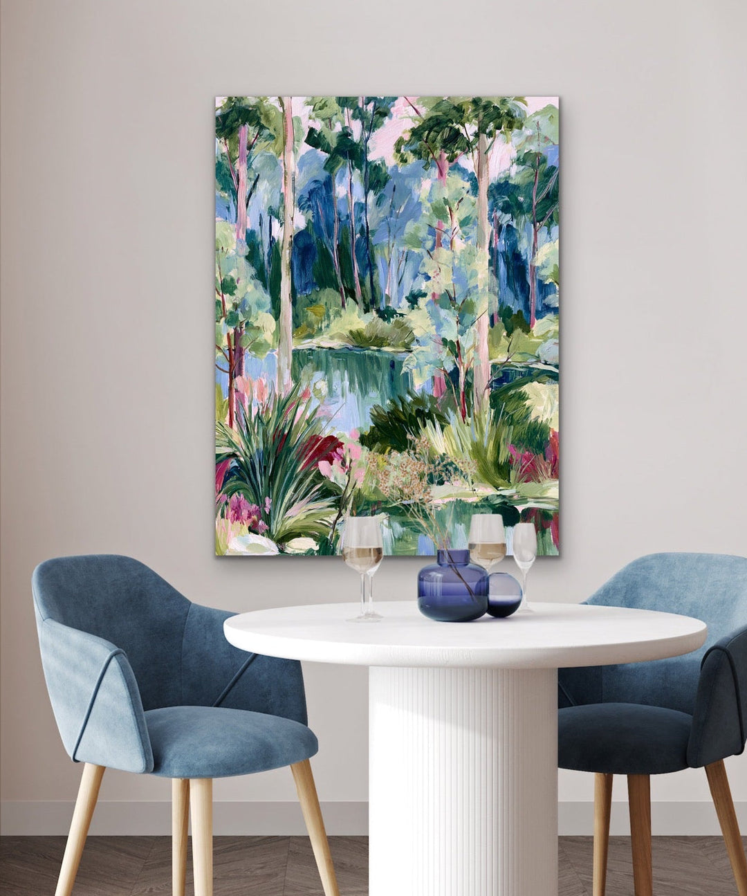 Dining room with a round table and blue chairs, featuring a colorful abstract painting on the wall.