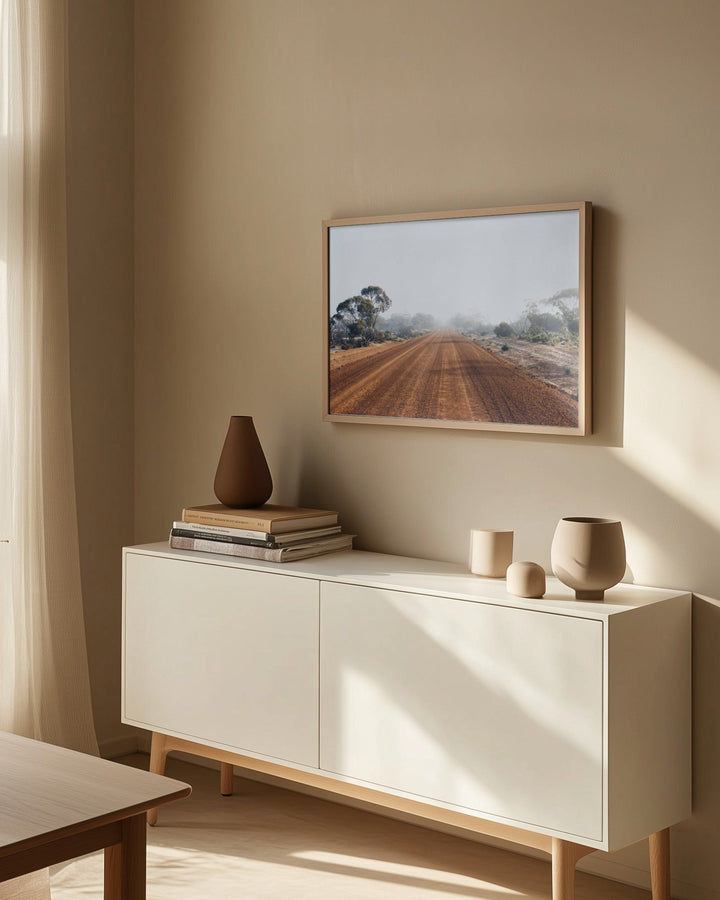 A sleek minimalist white sideboard with light wood legs displayed with red dirt road australian outback landscape print