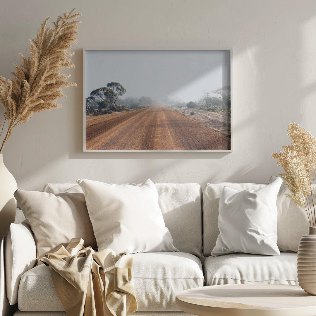 A framed photographic print of a dusty red dirt road in the australian outback under a hazy sky