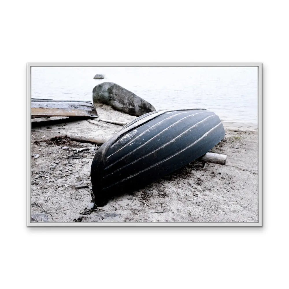 Rowboat on the shore stretched canvas photographic print featuring a black ribbed canoe resting on sandy shore