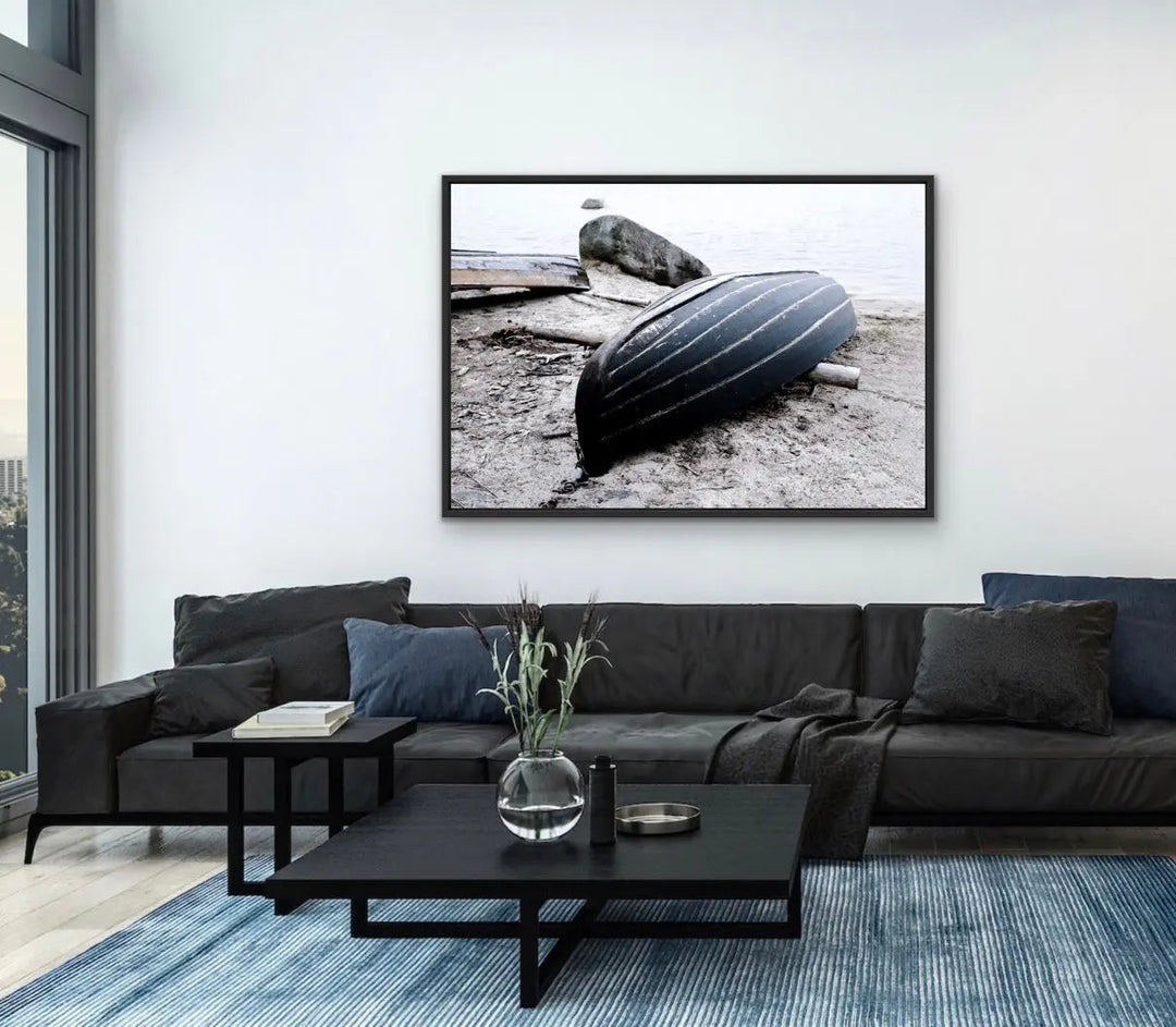 Black-framed black-and-white stretched canvas photographic print of a striped rowboat resting on a rocky shore