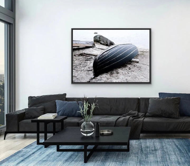 Black-framed black-and-white stretched canvas photographic print of a striped rowboat resting on a rocky shore
