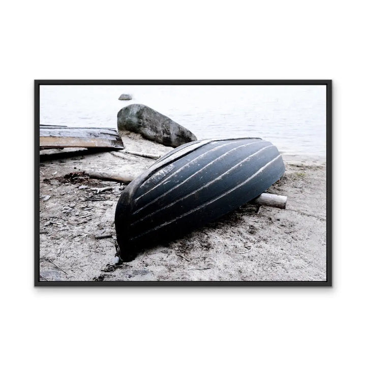 Rowboat on the shore stretched canvas photographic print featuring a black ribbed canoe resting on sandy shore